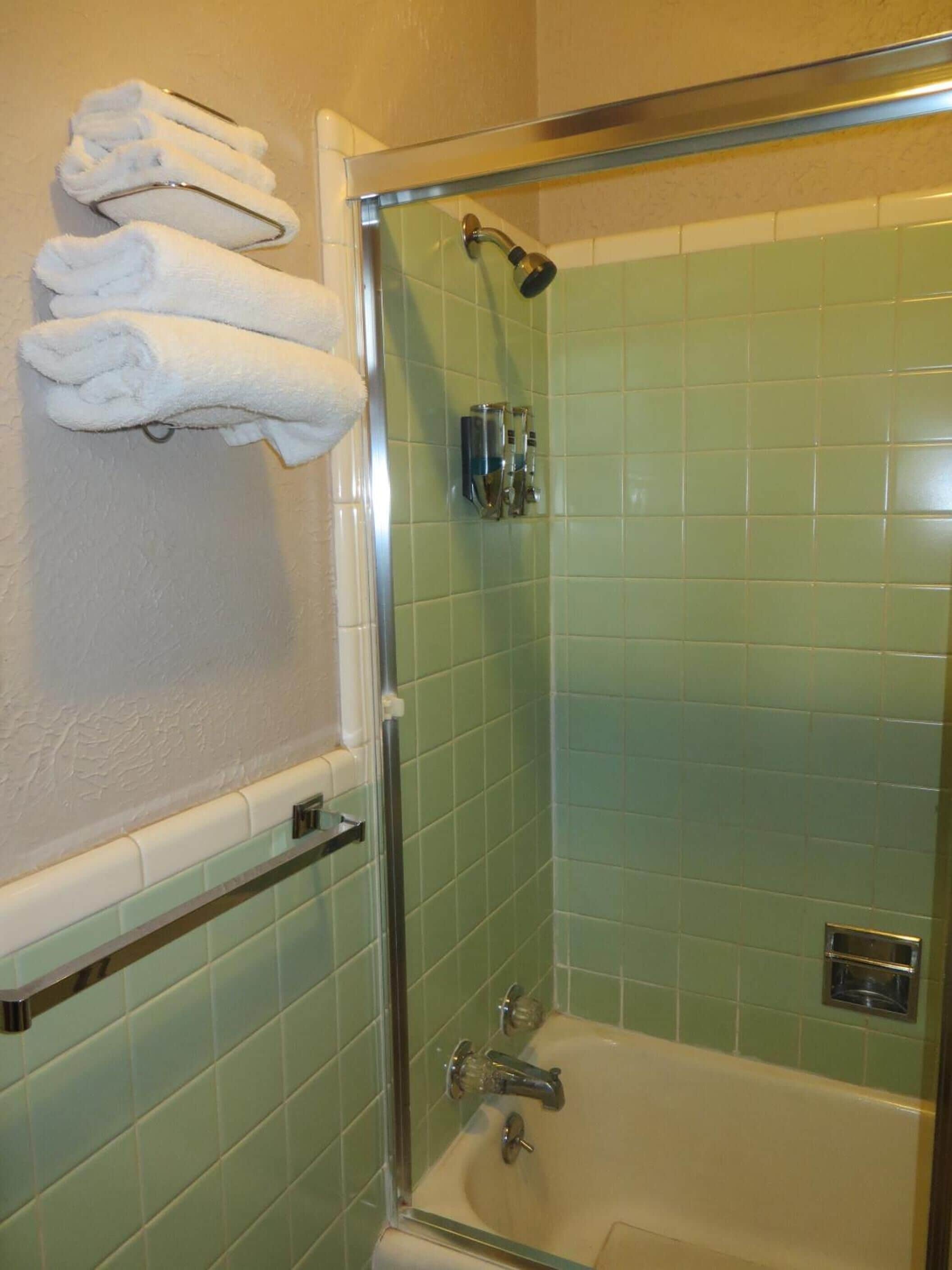A bathroom with a glass-enclosed shower, green-tiled walls, and a towel rack with folded towels.