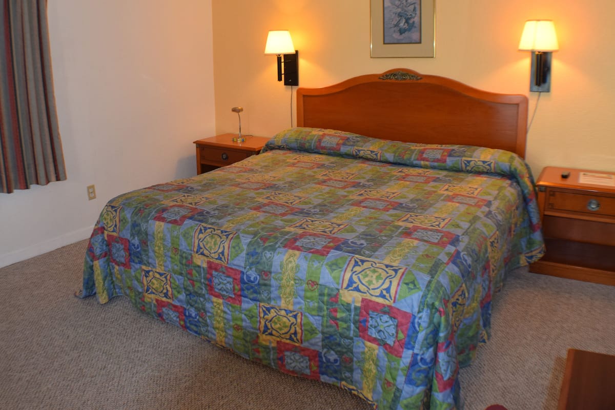 A neatly made bed with a colorful quilt, two bedside lamps, and a framed picture on the wall.