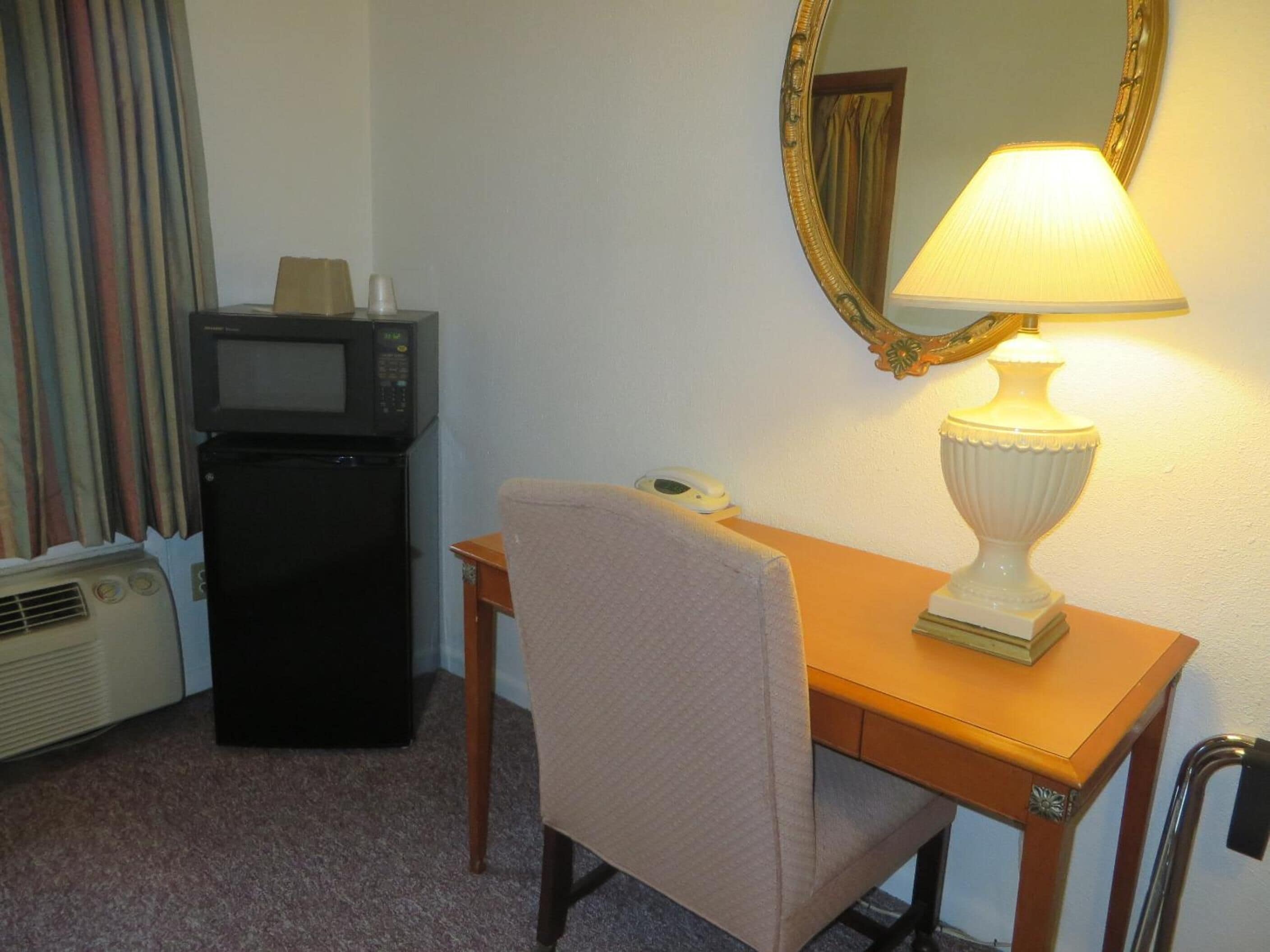 A hotel room with a desk, a lamp, a microwave, and a telephone.