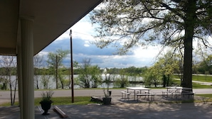 A covered outdoor area with picnic tables and benches, a view of a lake, and a paved path.
