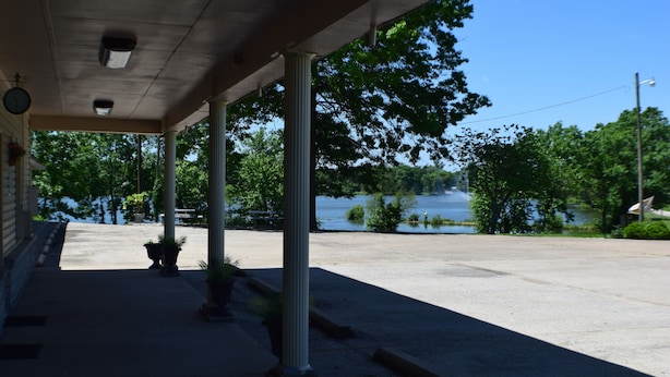 A covered outdoor area with columns, potted plants, and a view of a lake.