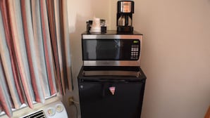 A compact kitchenette with a microwave and a refrigerator, a coffee maker on the microwave, and a vent on the refrigerator.