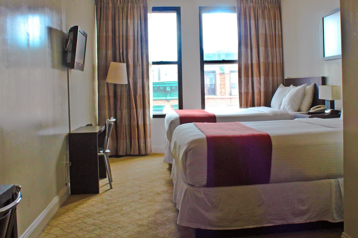 A hotel room with two beds, a desk, a chair, a TV, and a window with curtains.
