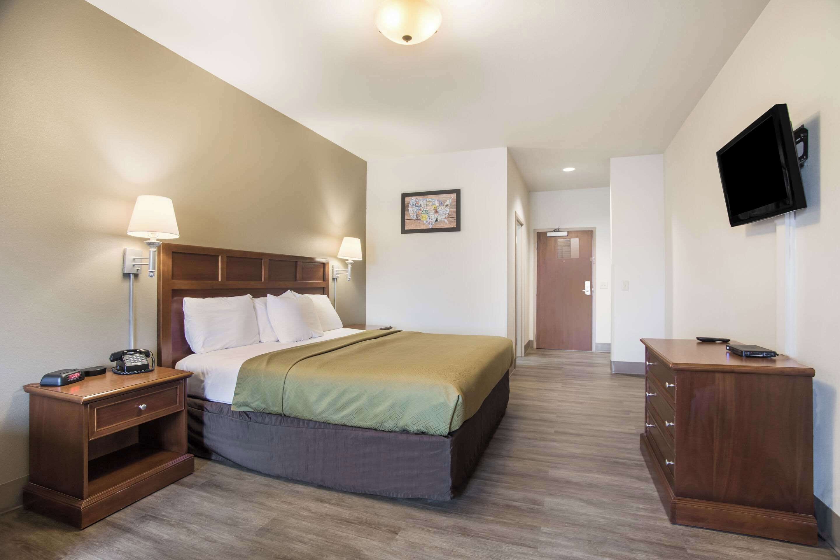 A hotel room with a bed, bedside lamps, a desk, a dresser, and a television on the wall.
