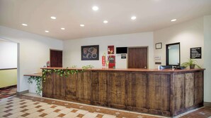 Un mostrador de recepción con detalles de madera, una zona de registro y una planta en maceta.