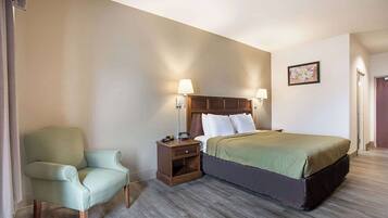Een hotelkamer met een bed, een stoel, een nachtkastje en een lamp.