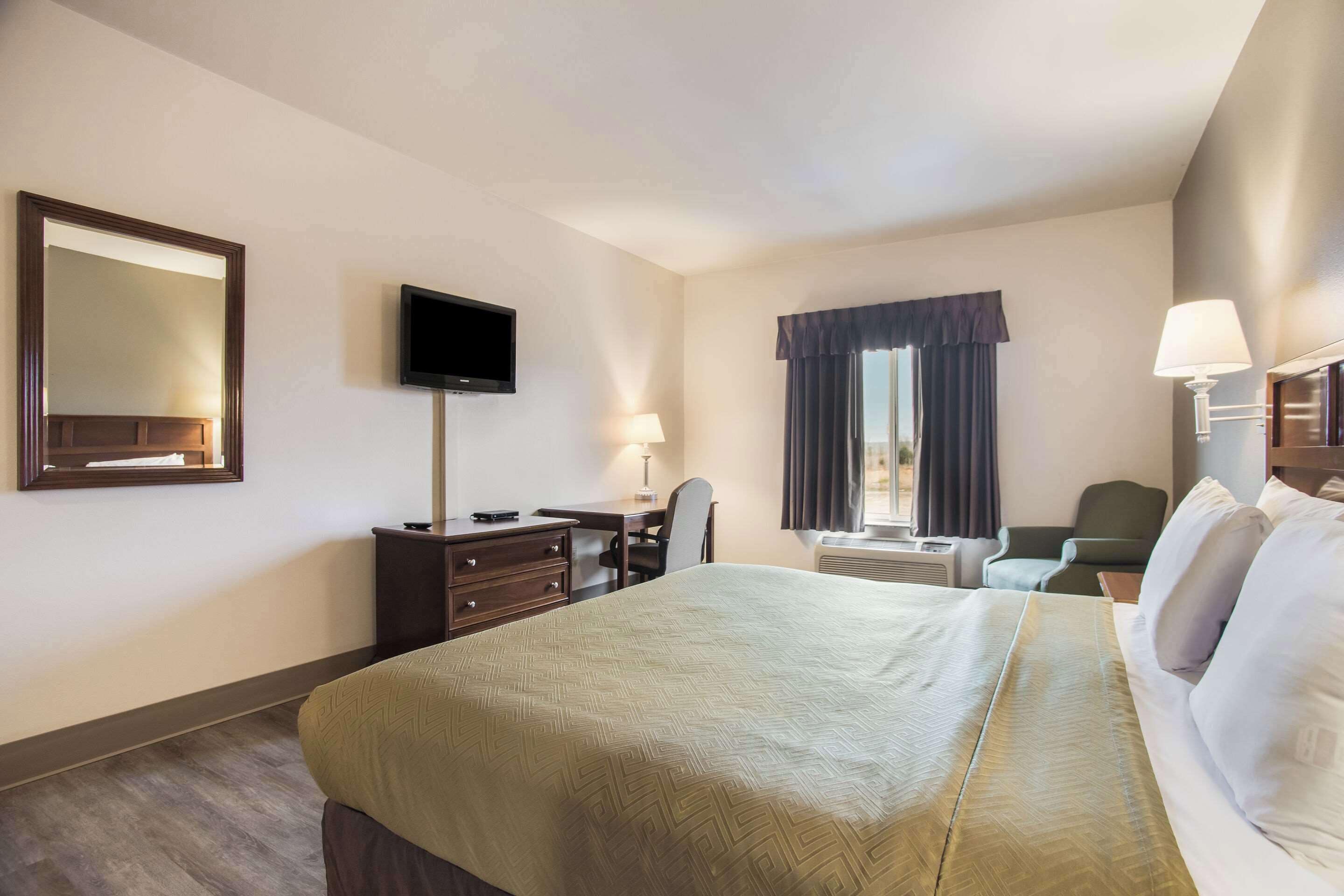 A hotel room with a large bed, a desk with a chair, a television, and a window with curtains.