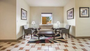 Una sala de estar con un sofá, dos sillones, una mesa de centro y un tapete estampado. Se observan cuadros en las paredes y una ventana con vistas a árboles.