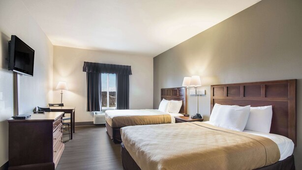 Una habitación de hotel con dos camas, un escritorio, un televisor y una ventana con cortinas.