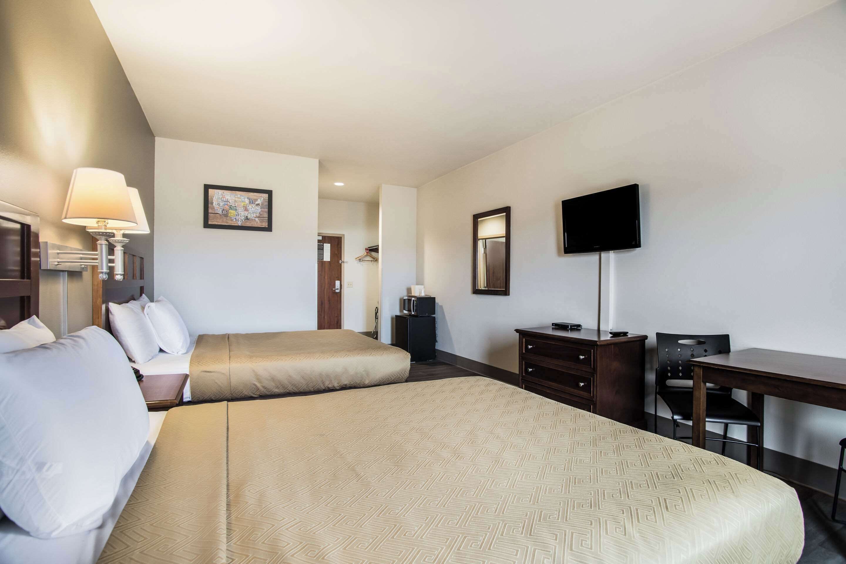 Quarto de hotel com duas camas, uma escrivaninha, uma cadeira, uma televisão e um espelho.