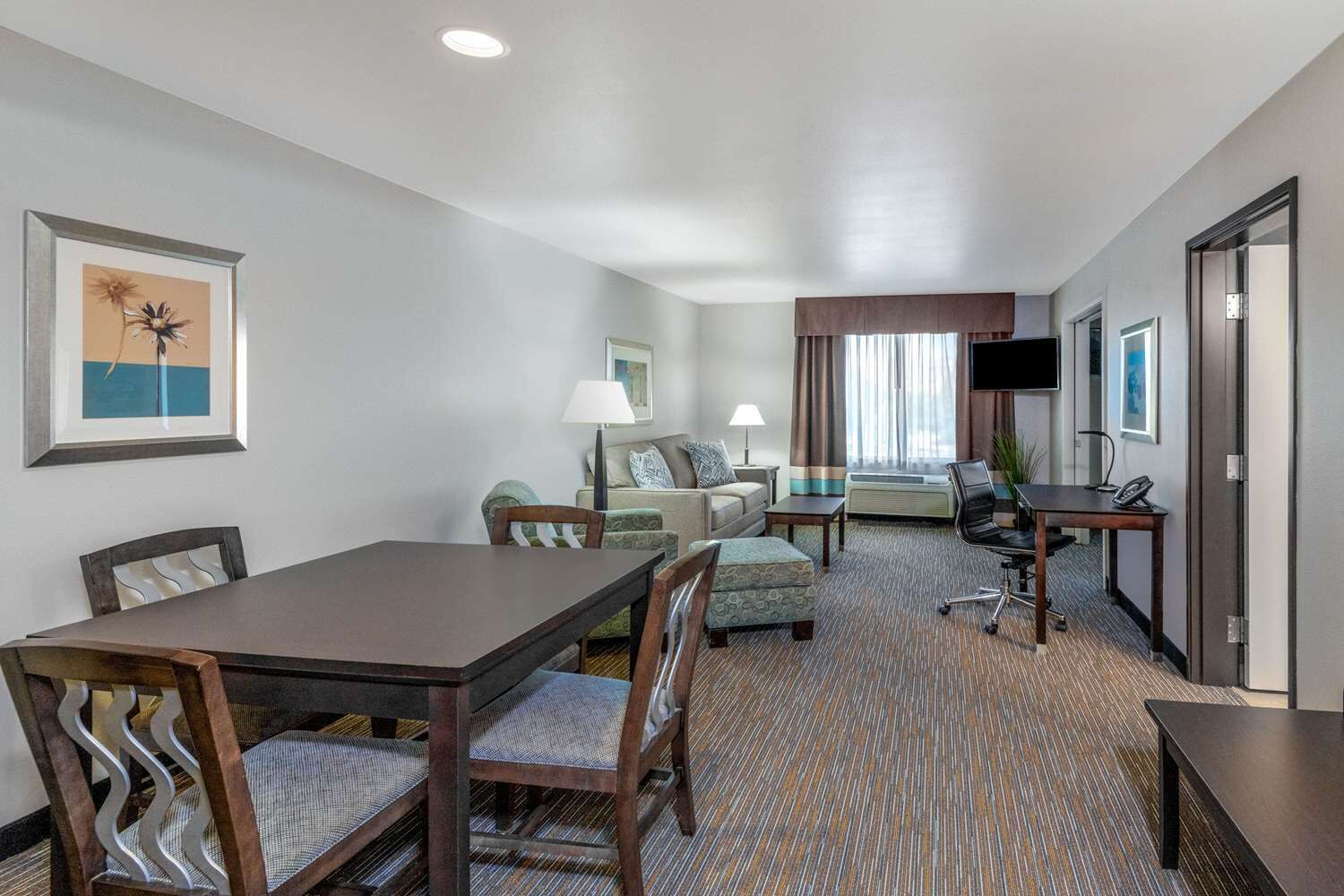 A hotel room with a dining table, two sofas, a TV, and a desk with a chair.