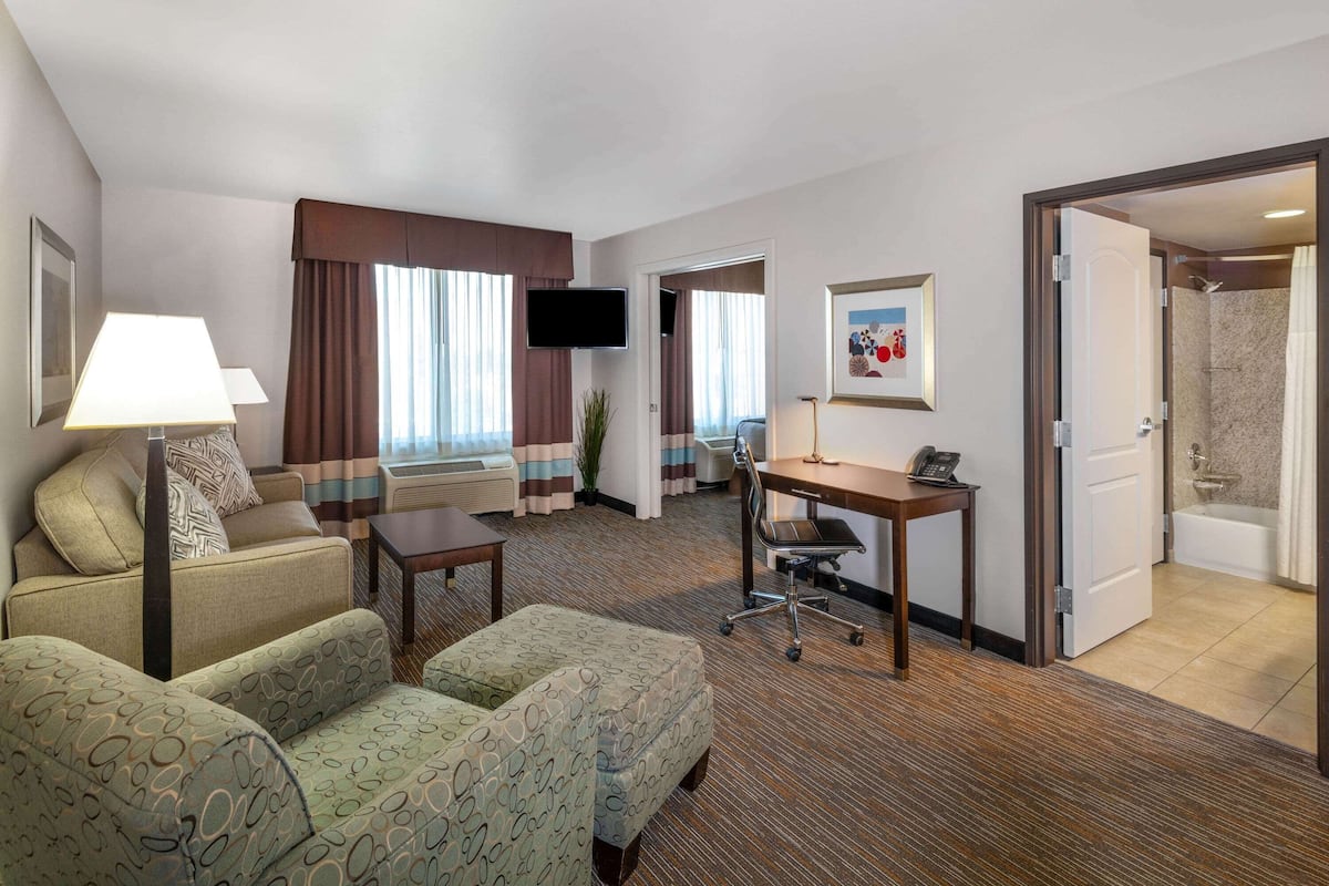 A hotel room with a sofa, a desk, a TV, and a bathroom visible through an open door.