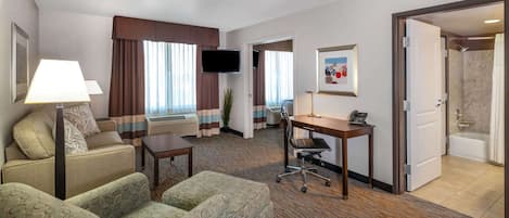 Habitación de hotel con sofá, escritorio, televisión y baño visible a través de una puerta abierta.