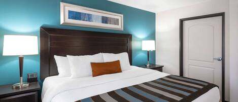 A hotel room with a large bed, two bedside tables with lamps, a framed artwork above the bed, and a door to the right.