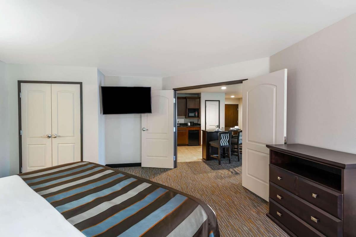 A hotel room with a bed, a TV, a desk with chairs, and a kitchenette.