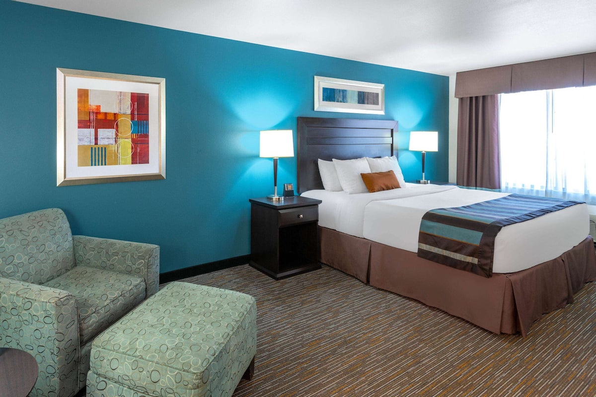 A hotel room with a large bed, two bedside tables, a chair, and a framed abstract painting on the wall.
