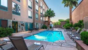 A hotel pool area with sun loungers, a swimming pool, palm trees, and a stone building facade. - Wingate by Wyndham St. George (St. George)
