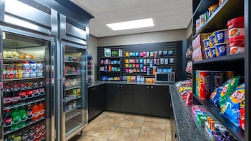 A grocery store interior with refrigerated sections on the left, shelves stocked with snacks and beverages, and a checkout counter in the center.