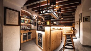Een bar met houten meubels, een hoog plafond met zichtbare balken en diverse flessen op planken.
