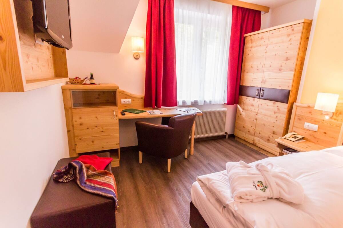 Une chambre d’hôtel de taille réduite, comprenant un lit, un bureau, une chaise, une armoire et un téléviseur.
