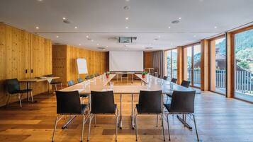 Un salón de conferencias con una larga mesa, sillas negras, paredes de madera y ventanas amplias.