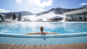 Iemand ontspant in een jacuzzi met uitzicht op een besneeuwde berg en een gebouw op de achtergrond.