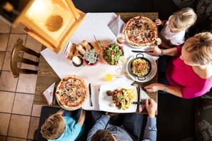 Een gezin dineert aan een tafel met pizza, salade en pasta.