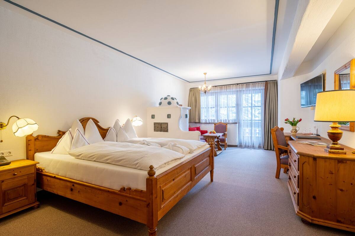 Une chambre d’hôtel avec un lit en bois, un bureau avec une lampe, une chaise et une vue sur la ville grâce à de grandes fenêtres.