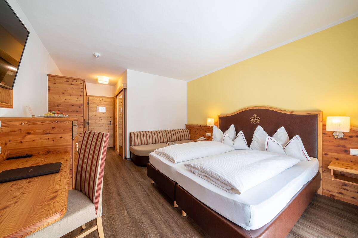 Une chambre d’hôtel avec un grand lit, un bureau en bois, une chaise, un banc et un téléviseur.