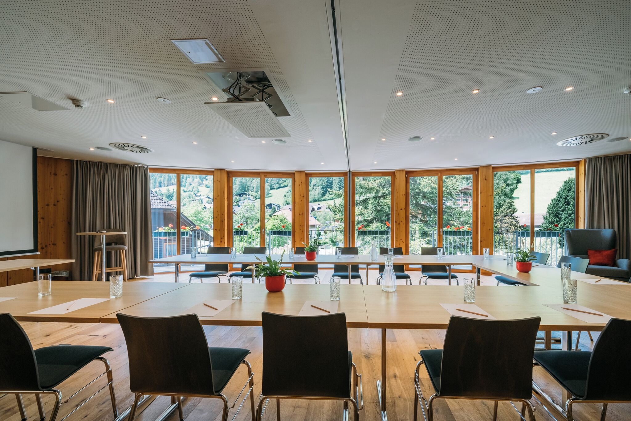 Uma sala de conferências com uma mesa comprida, cadeiras e grandes janelas com vista para árvores e edifícios.