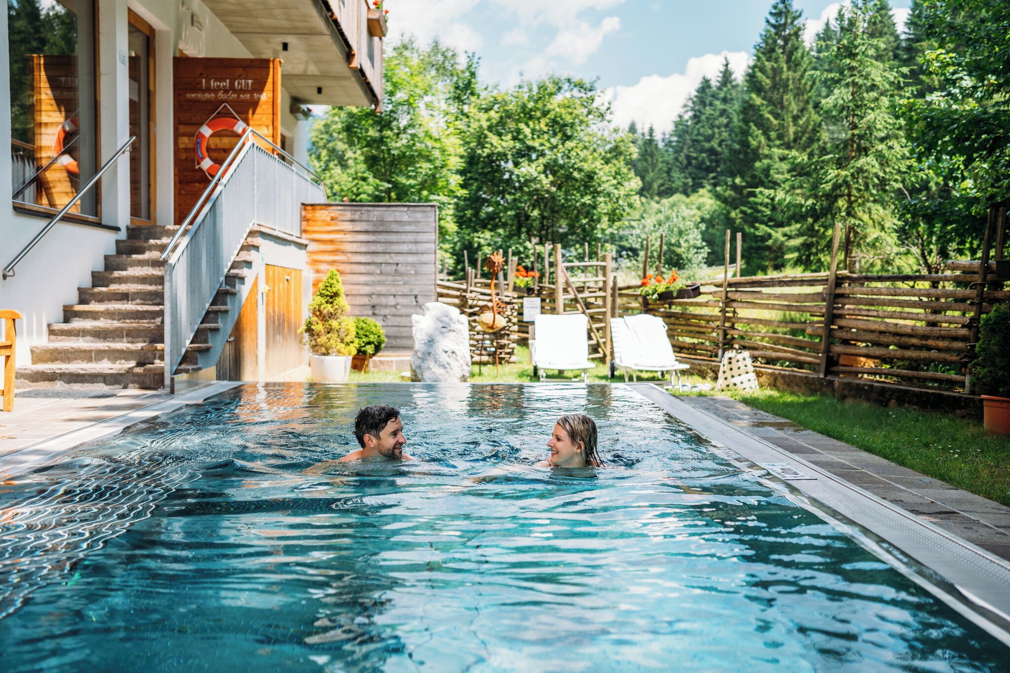 Una piscina con muelle de madera, pared de piedra y vista a árboles.