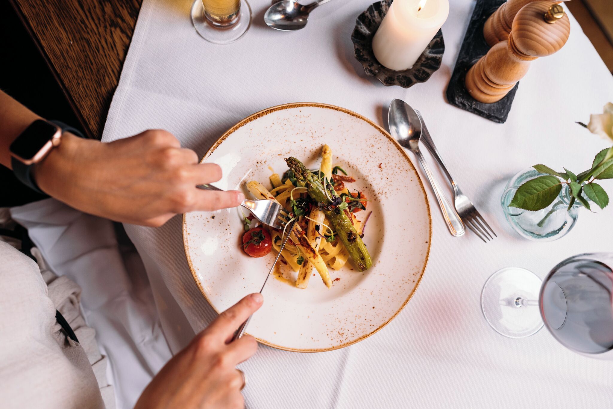 A dining table with a plate of food, utensils, and a glass of wine.