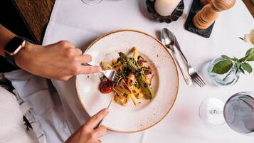 A dining table with a plate of food, utensils, and a glass of wine.