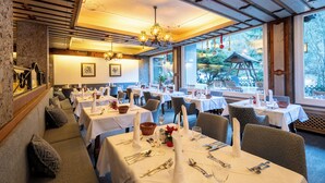Een restaurant met gedekte tafels, een houten plafond en grote ramen met uitzicht op groen.