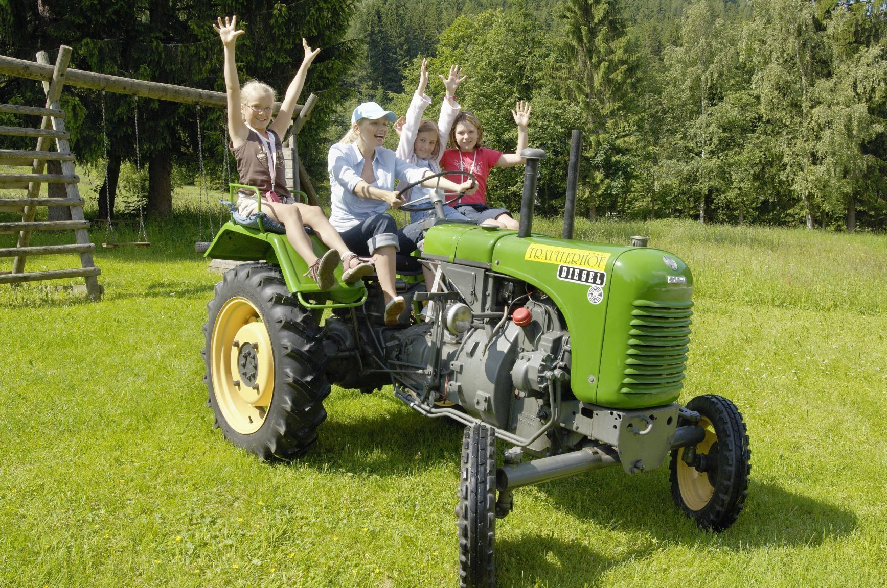 A green tractor with four people on it, raising their hands in excitement.