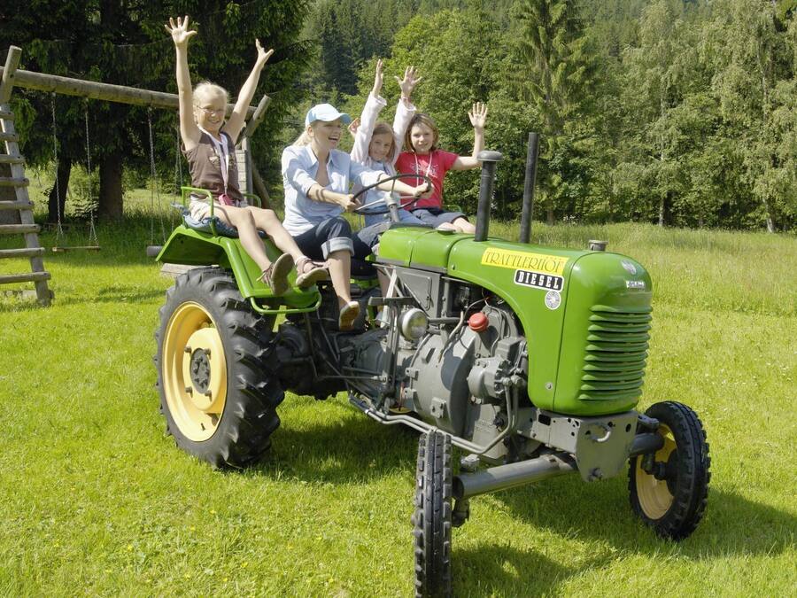 A green tractor with four people on it, raising their hands in excitement.