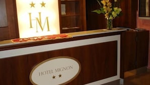 A reception desk with a sign reading "HOTEL MIGNON" and a logo with three stars above the letter "M". - Hotel Mignon (Alassio)