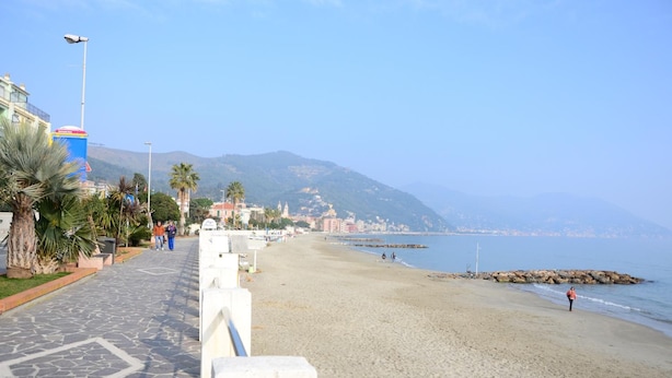 A coastal walkway with a beach, palm trees, and buildings in the background. - Hotel Mignon (Alassio)