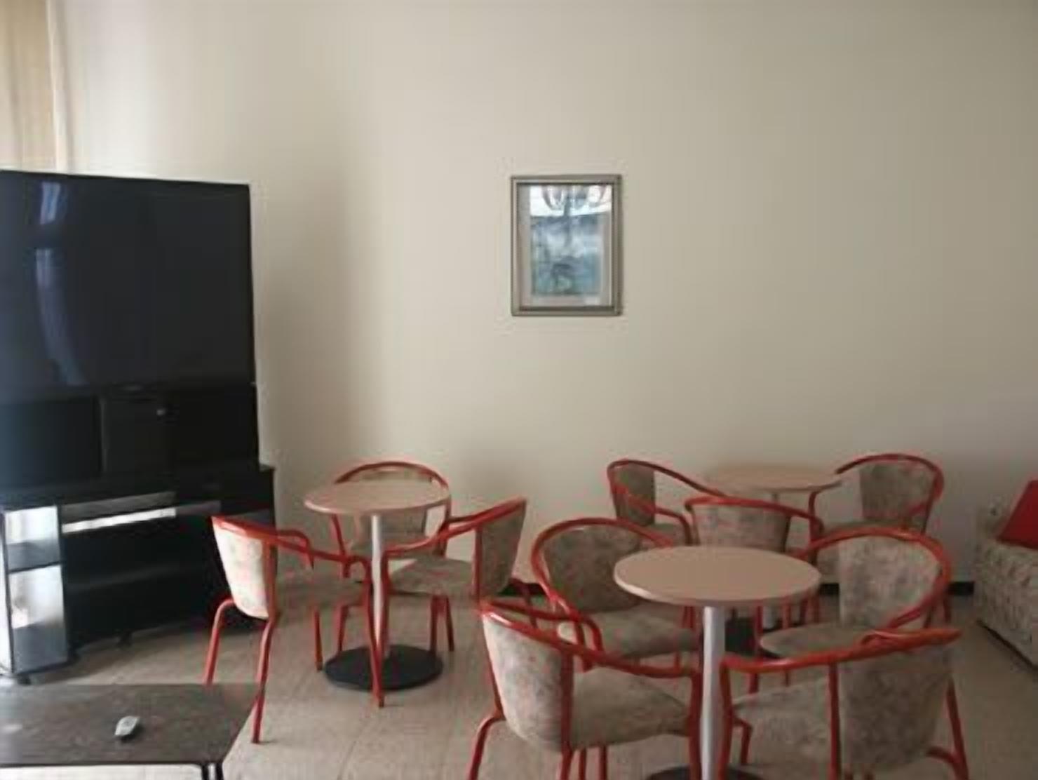 Un soggiorno con una televisione a schermo piatto, un tavolino rotondo e diverse poltrone rosse.