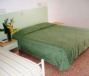 A single bed with a green bedspread in a room with a white headboard and a nightstand with a vase of flowers. - Hotel Mignon (Alassio)