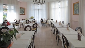A dining area with multiple tables and chairs, a chandelier, and framed artwork on the walls. - Hotel Mignon (Alassio)