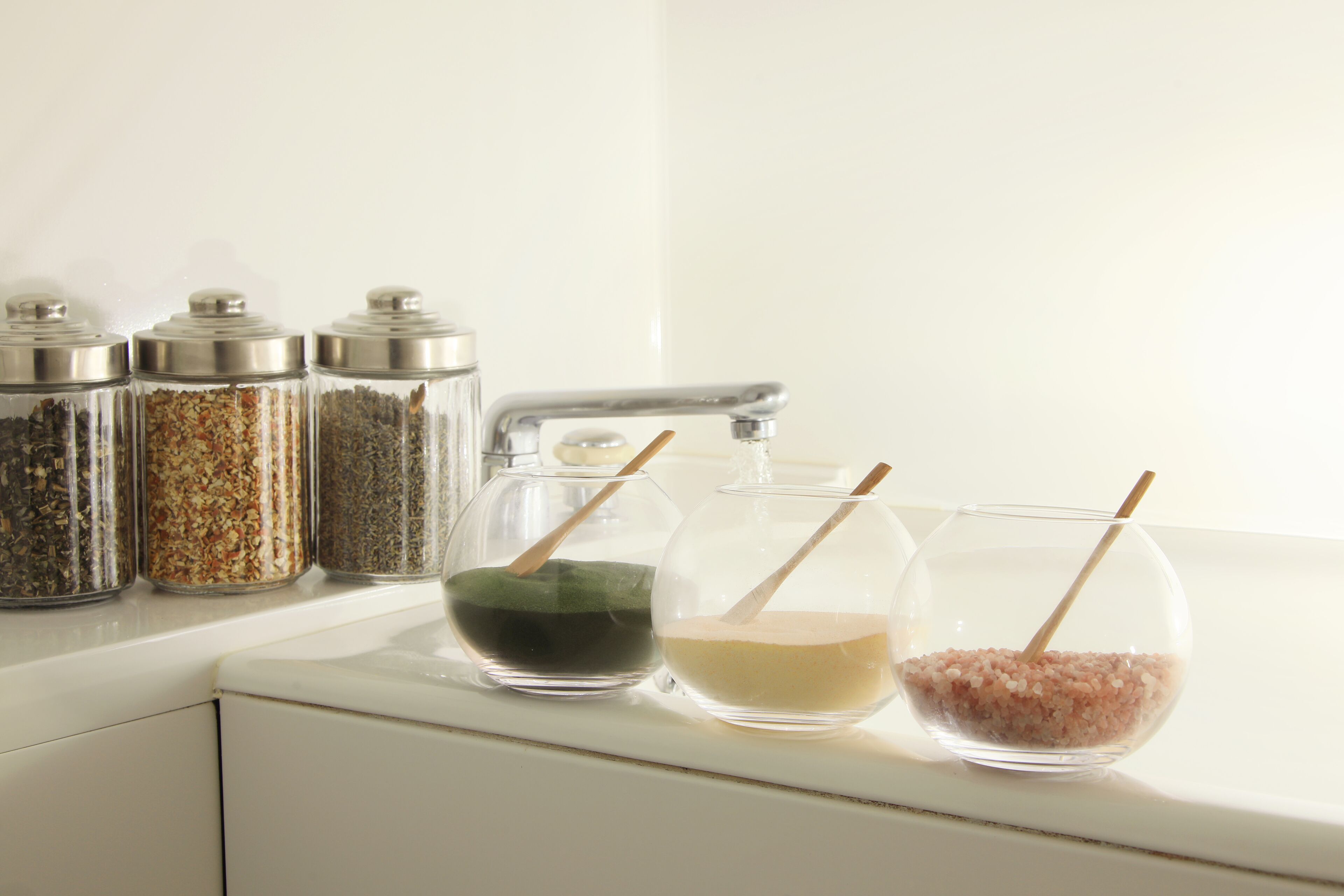 Una encimera de cocina con tres recipientes de vidrio y dos cuencos de vidrio con cucharas de madera.