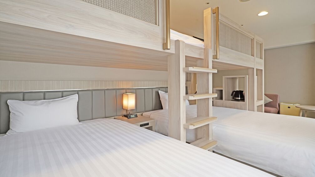 A hotel room with two beds, a nightstand with a lamp, a wooden ladder, and a small seating area.