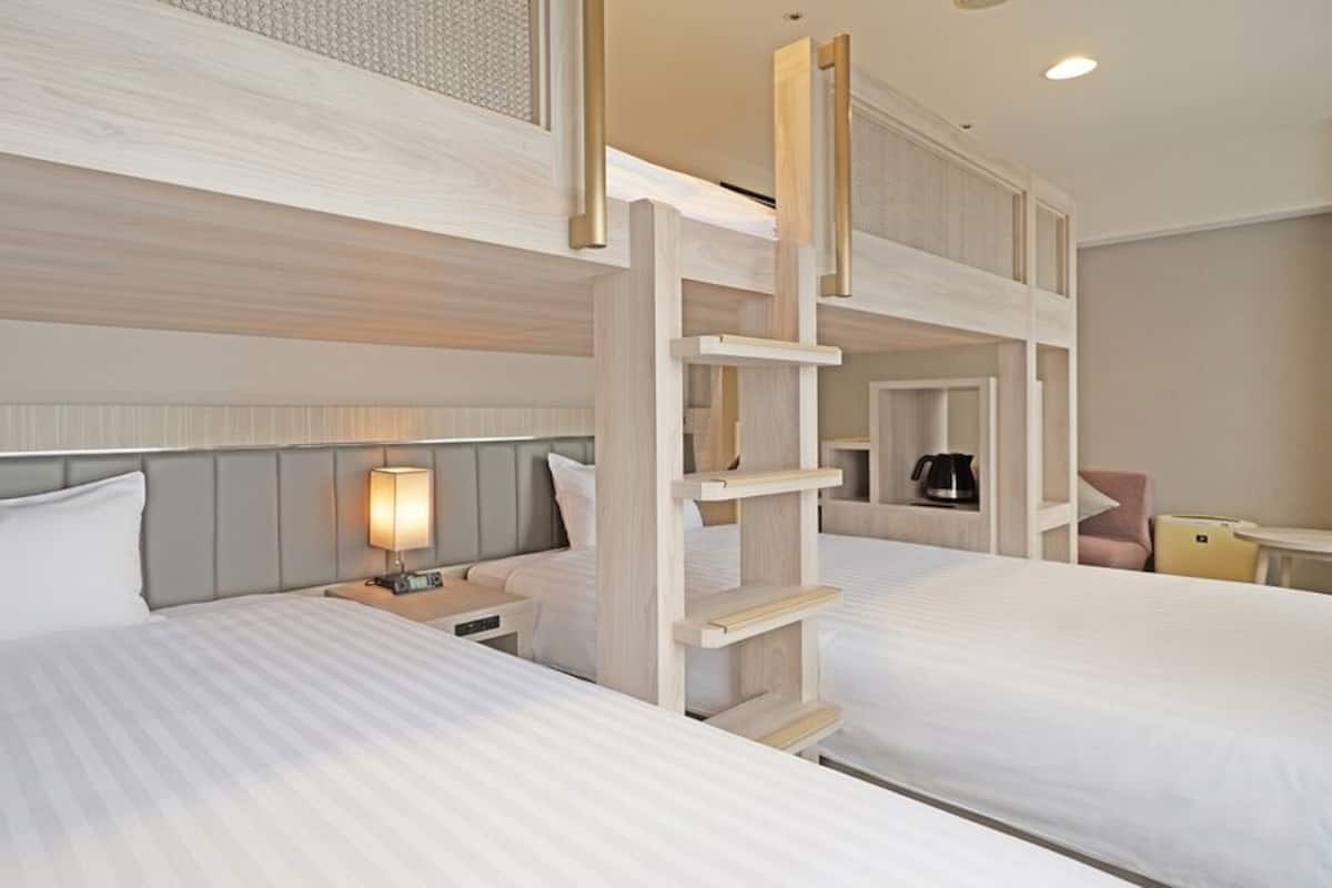 Une chambre d’hôtel avec deux lits, une table de chevet avec une lampe, une échelle en bois et un petit coin salon.