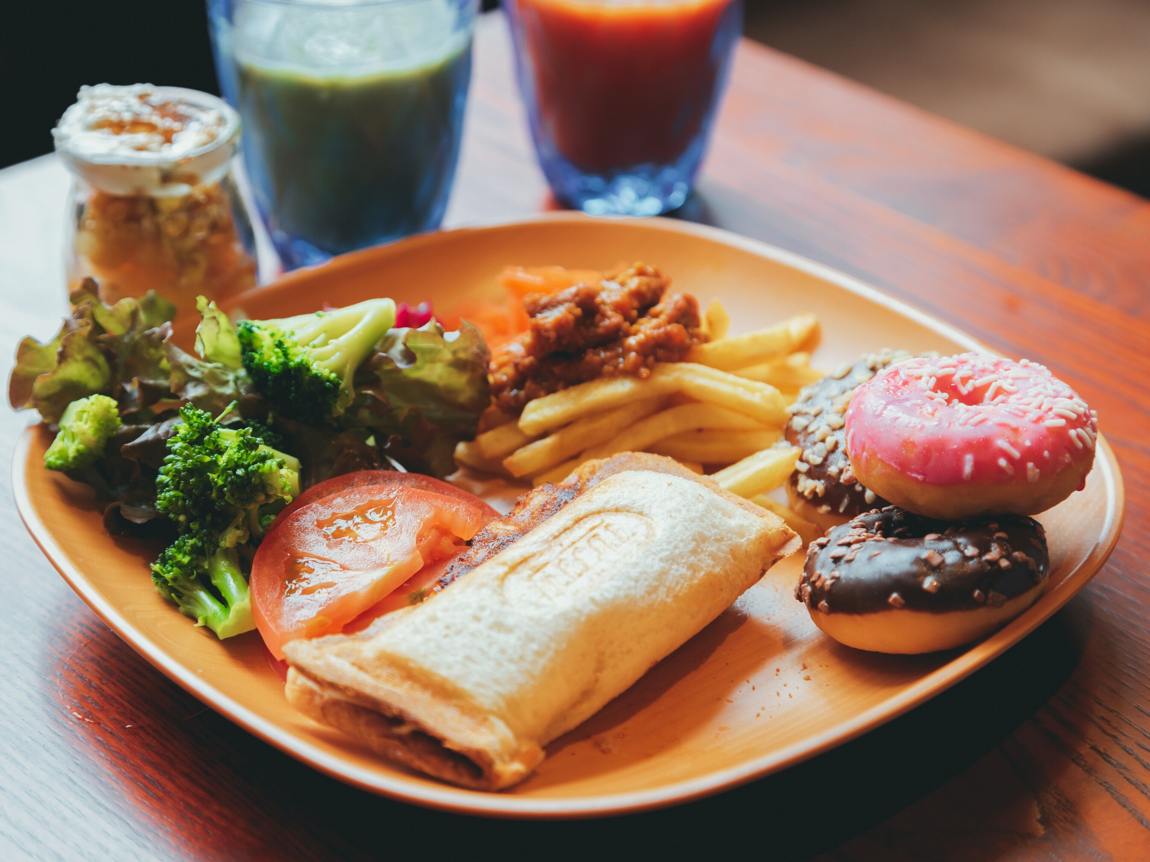 A plate of food including a sandwich, fries, a donut, and vegetables.