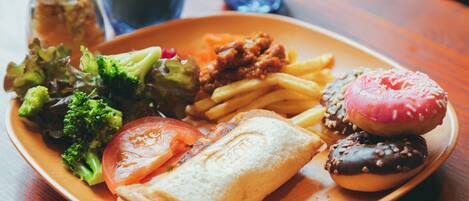 A plate of food including a sandwich, fries, a donut, and vegetables.