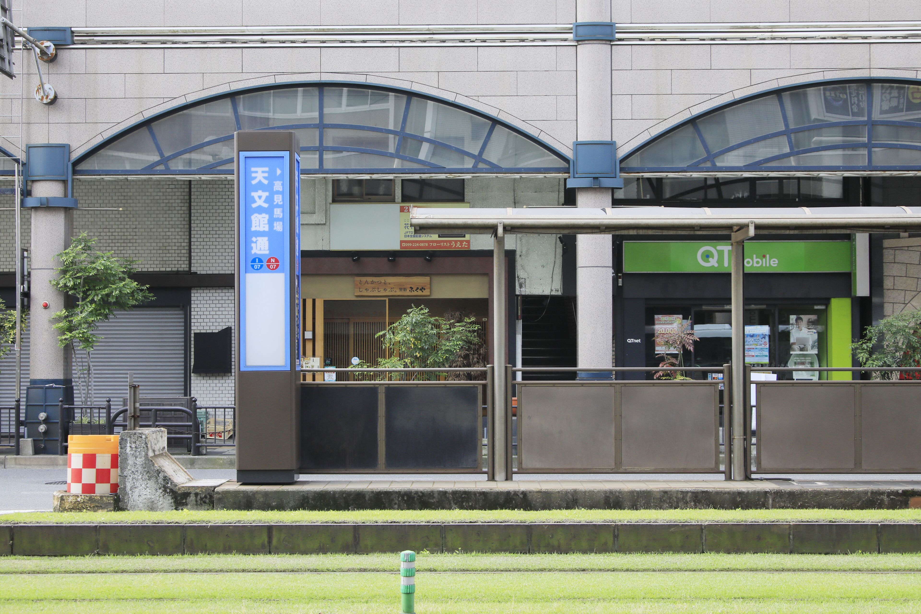 A train station with a blue sign, a Q1 Mobile store, and a closed shop.
