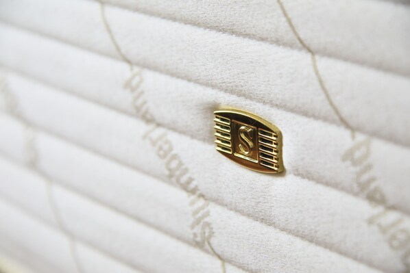 Primer plano de un objeto dorado con diseño de cerradura, sobre una superficie blanca con textura y líneas horizontales.