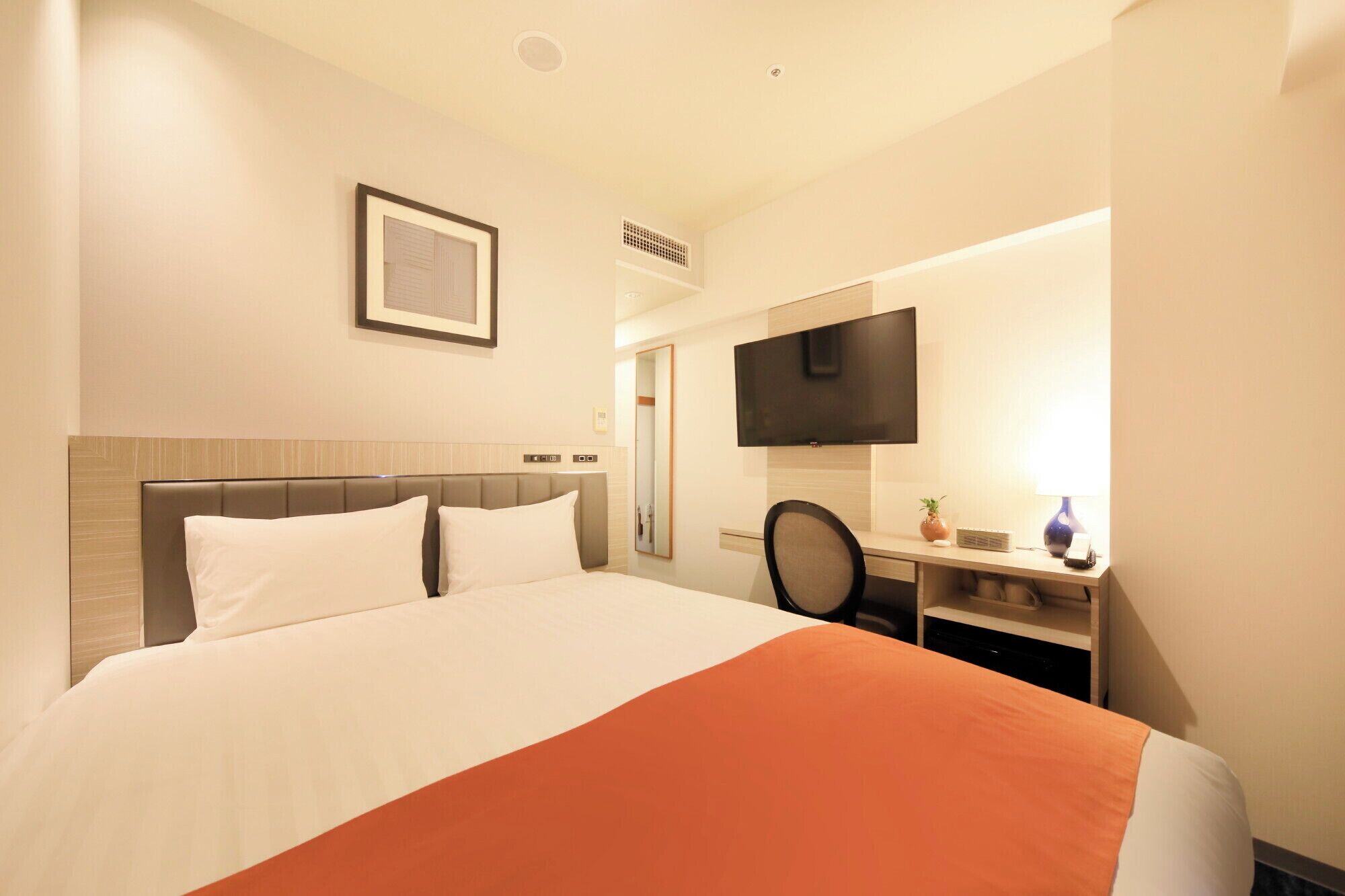 A hotel room with a bed, a desk, a television, and a mirror.
