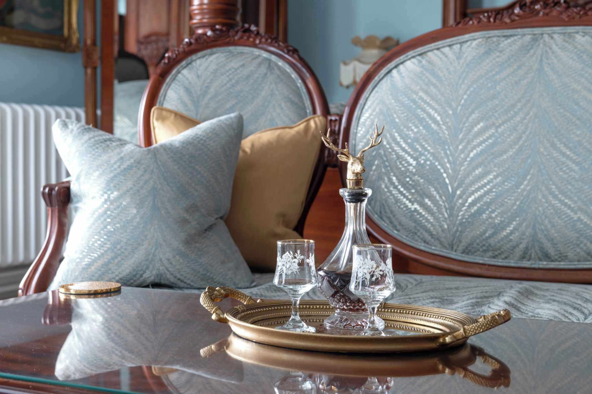 A bed with a headboard, a bedside table with a tray holding glasses and a bottle, and a pillow on the bed.